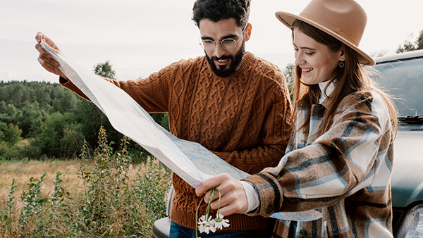 A man and a woman in the countryside reading a map next to a car.